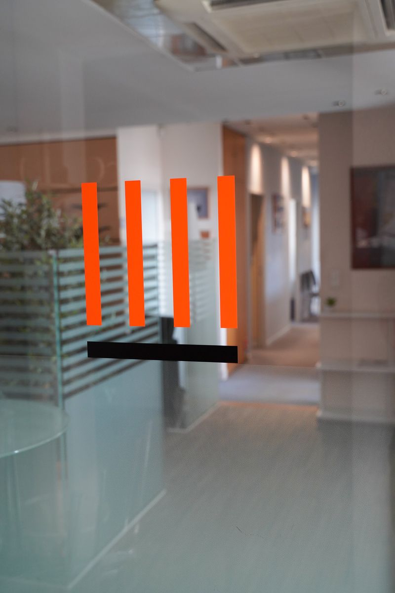 Logo du cabinet, quatre barres orange, sur la porte vitrée du couloir